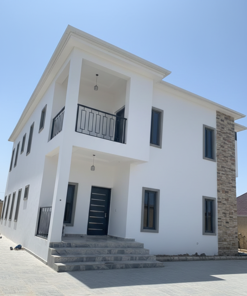 A completed modern two-story white house with grey window frames, a balcony, and decorative stone wall cladding.